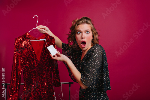 Εκτύπωση καμβά Shocked young woman looking at the price tag on red dress