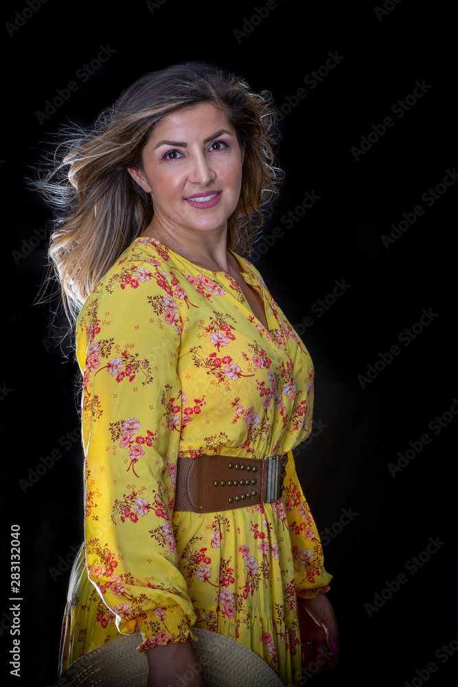 Fashionable Brunette with Flowy Hair Wearing a Floral Yellow Dress in Studio with a Black Backdrop Fashionable Brunette with Flowy Hair Wearing a Floral Yellow Dress in Studio with a Black Backdrop