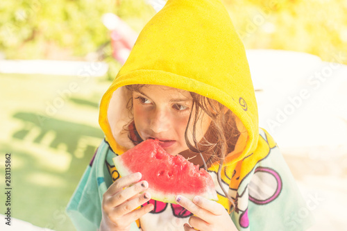 Close up of a little girl in her beach towel, eating watermelon on the poolside