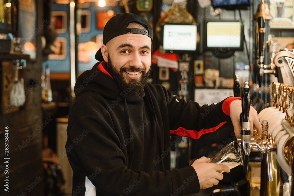 Smiling bearded barman pours beer into a glass. Friendly man working at the bar Smiling bearded barman pours beer into a glass. Friendly man working at the bar
