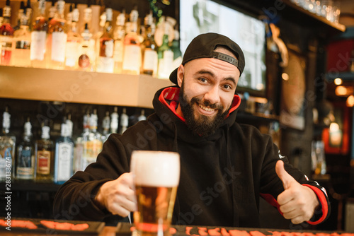 Smiling bearded bartender gives beer in a glass. Friendly man working at the bar