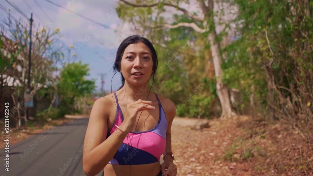 frontal pull back gimbal shot in dolly style of young exotic fit and beautiful Asian Indonesian woman running on asphalt road doing jogging workout in sport and healthy lifestyle concept frontal pull back gimbal shot in dolly style of young exotic fit and beautiful Asian Indonesian woman running on asphalt road doing jogging workout in sport and healthy lifestyle concept