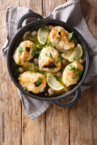 Greek cuisine cod steaks with lemon and olives closeup in a pan. Vertical top view
