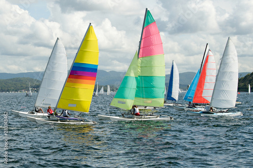 Children Sailing small sailboats with colourful sails on an inland waterway.