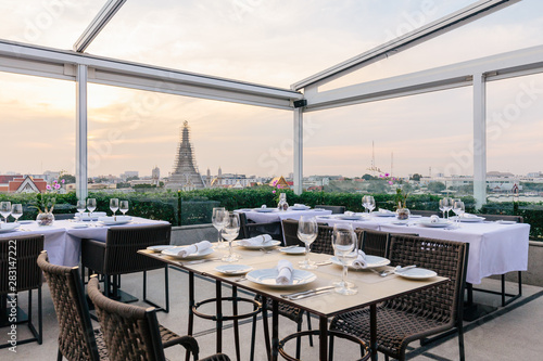 Photography Renovated Wat Arun (The Temple of Dawn) with boats moving over Chaophraya river that view from restaurant with dining tables in the evening in Bangkok, Thailand