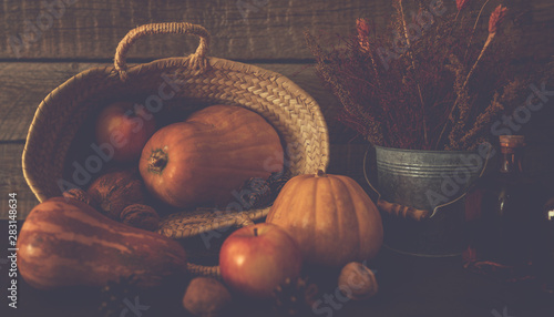 Colored fall vegenables on the vintage boards. Autumn decorations in wicker basket. A cornucopia with squash, gourds, pumpkins, cones, wheat and leaves. Toned image with copy space. Harvest time. photo