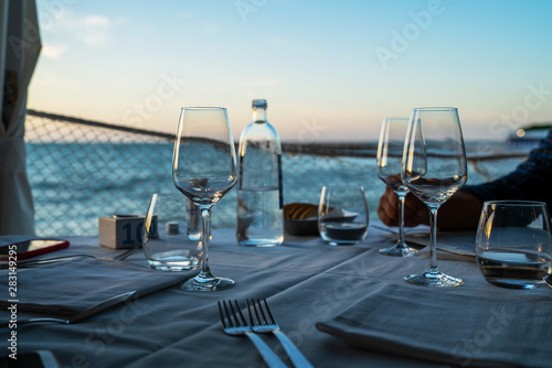 Beautiful outdoor restaurant interior. Empty wine glasses on the blurred sea view background. Elegant restaurant table waiting for customers by the sea outdoor terrace in Portonovo,Italy.