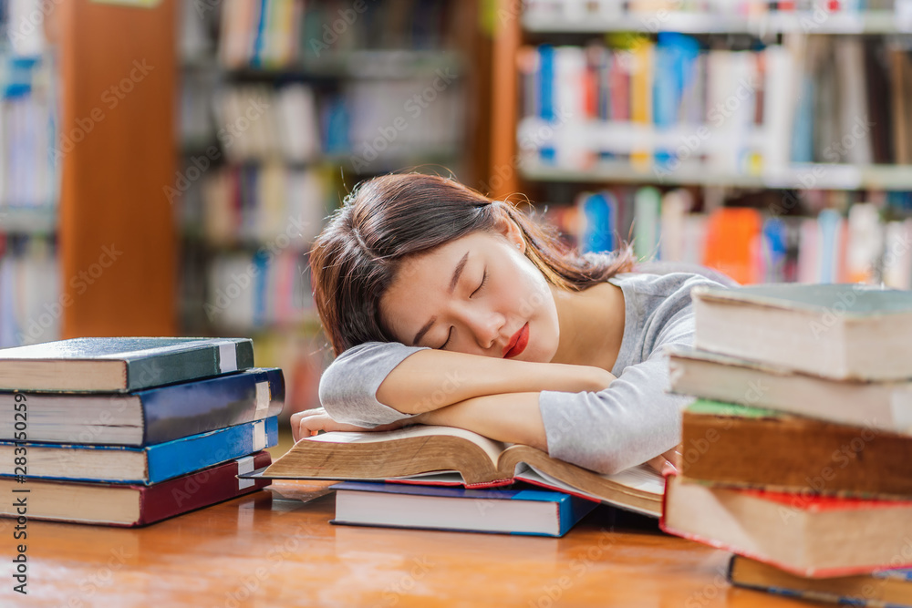 Asian young Student in casual suit reading and sleeping on the wooden table with various book in library of university or colleage over the book shelf, Back to school concept Asian young Student in casual suit reading and sleeping on the wooden table with various book in library of university or colleage over the book shelf, Back to school concept