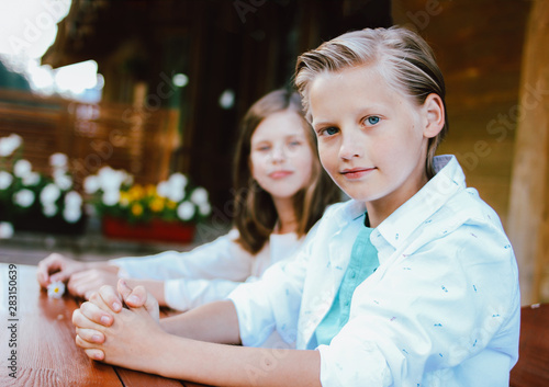 Fotografie Attractive preteen blonde boy with blue eyes in white shirt with sister friend s