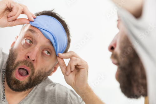 Sleepy man looking at mirror and yawning