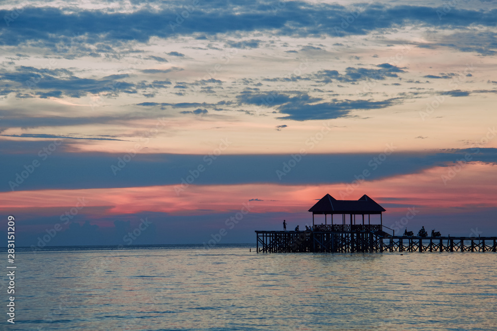 silhouettes of wooden pier and people at tropical sunset