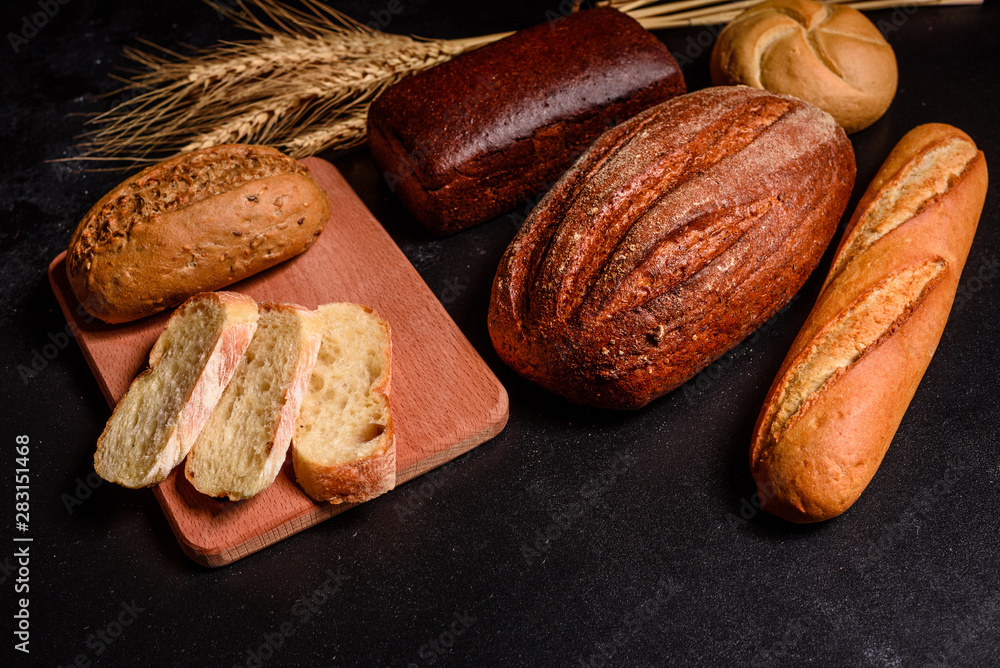 Obraz premium Fresh fragrant bread with grains and cones of wheat against a dark background. Assortment of baked bread on wooden table background. Fresh fragrant bread on the table. Food concept. 