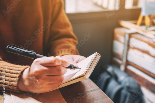 Closeup image of a woman holding and writing on blank notebook with fountain pen on wooden table