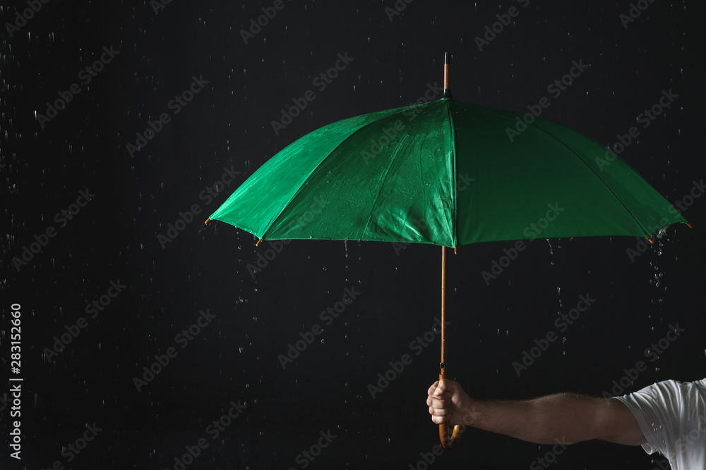 Man holding green umbrella under rain against black background ...