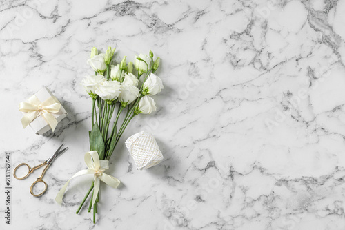 Flat lay composition with scissors and flowers on white marble background, space for text