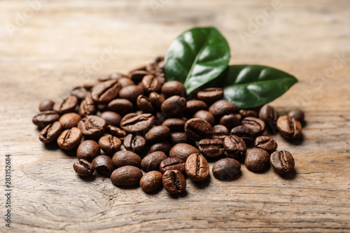 Pile of coffee beans and fresh green leaves on wooden table