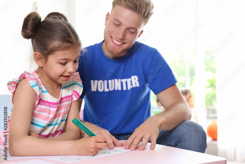 Little girl learning alphabet with volunteer at table indoors Little girl learning alphabet with volunteer at table indoors