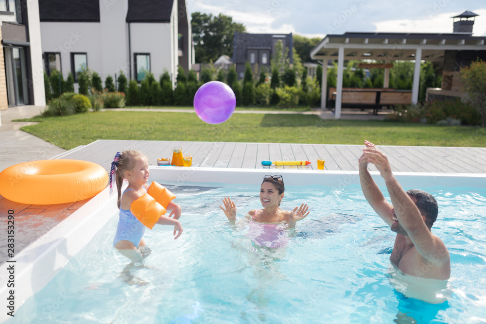 Girl feeling happy while playing ball with parents in the pool