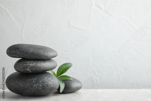 Stack of spa stones and green leaves on grey table, space for text