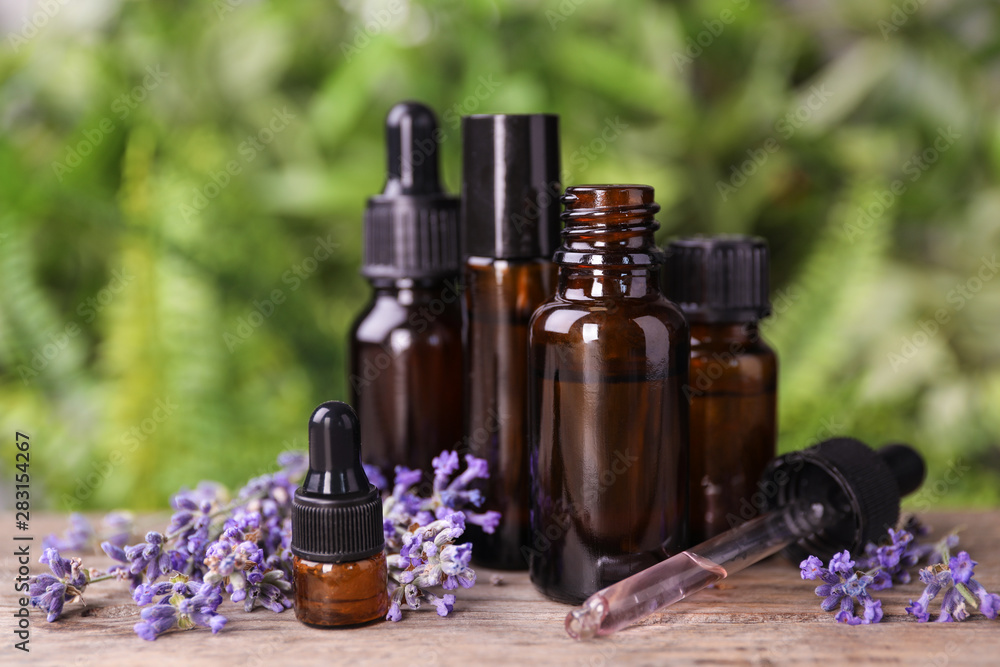 Bottles with natural lavender essential oil on wooden table against blurred background Bottles with natural lavender essential oil on wooden table against blurred background