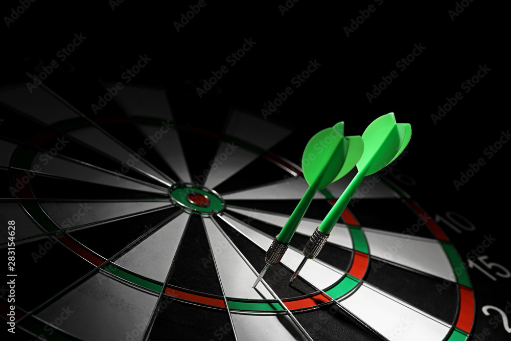 Green arrows hitting dart board against black background. Space for text Green arrows hitting dart board against black background. Space for text