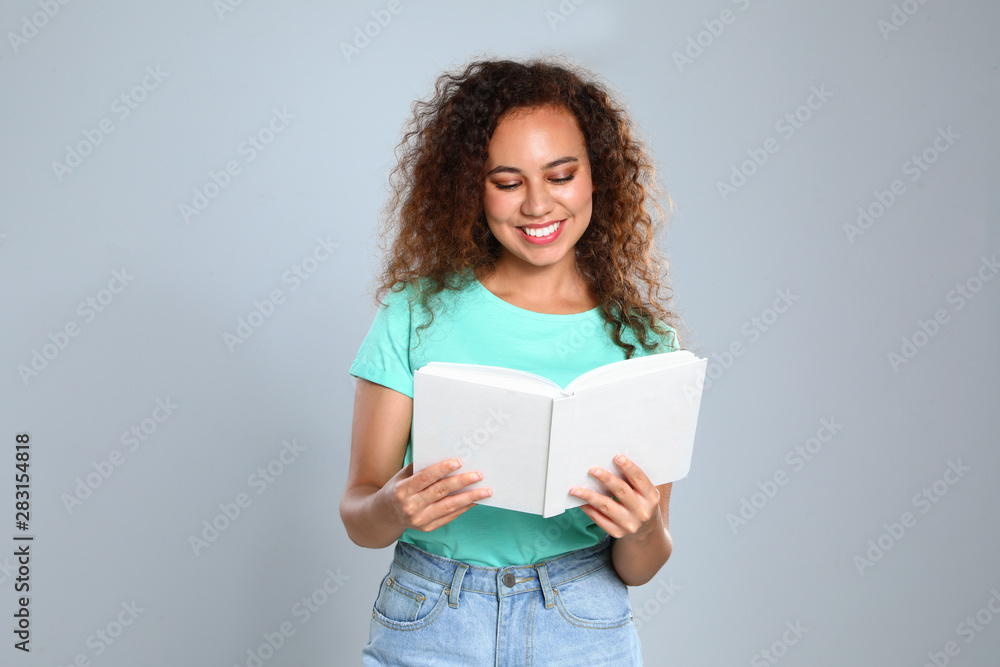 Beautiful African-American young woman reading book on light background Beautiful African-American young woman reading book on light background