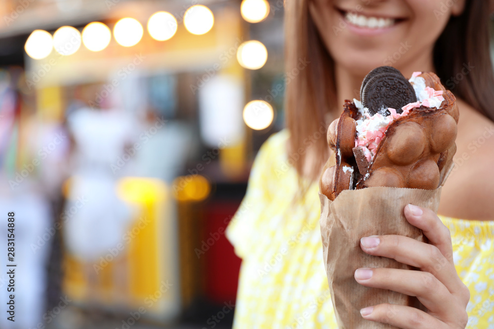 Young woman holding delicious sweet bubble waffle with ice cream outdoors, closeup - obrazy, fototapety, plakaty 