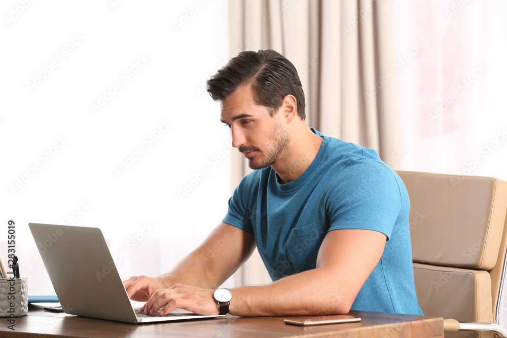 Handsome young man working with laptop at table in office Handsome young man working with laptop at table in office