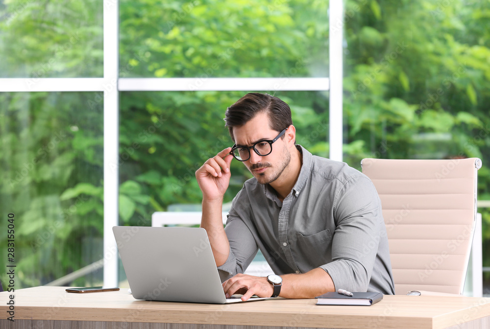 Handsome young man working with laptop at table in office Handsome young man working with laptop at table in office