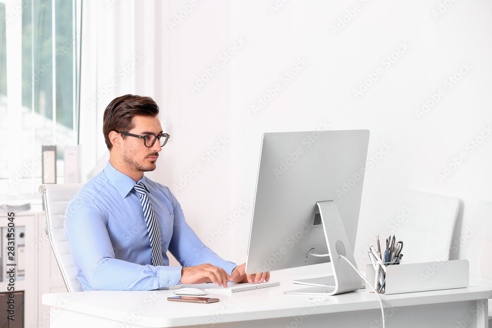 Handsome young man working with computer at table in office Handsome young man working with computer at table in office