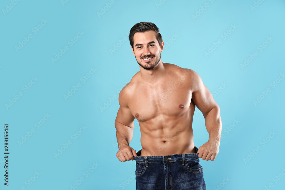Fototapeta premium Young man with slim body in old big size jeans on light blue background. Space for text