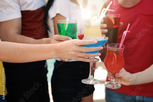 Friends clinking glasses with fresh summer cocktails outdoors, closeup