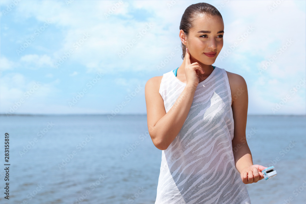 Young woman checking pulse with medical device after training on beach. Space for text Young woman checking pulse with medical device after training on beach. Space for text
