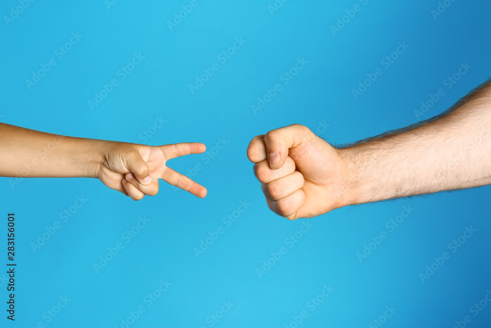 Little child and his father playing rock, paper and scissors on blue background, closeup Little child and his father playing rock, paper and scissors on blue background, closeup