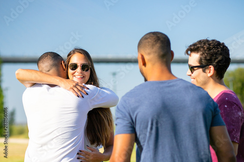 Smiling young people meeting at park and embracing. Group of friends greeting each other and laughing. Union concept