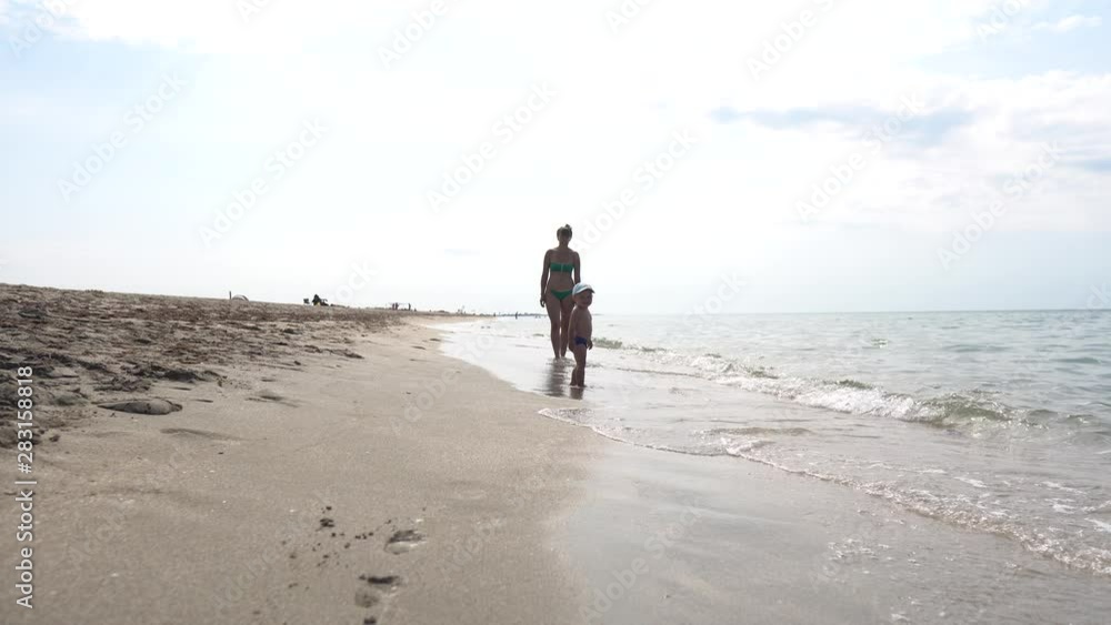 A young beautiful mother and her little boy walking on the sea coast and watching the waves A young beautiful mother and her little boy walking on the sea coast and watching the waves