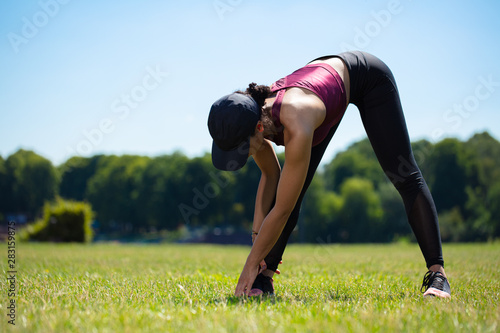 Girl doing stretch exercises outdoor in a park on a sunny day