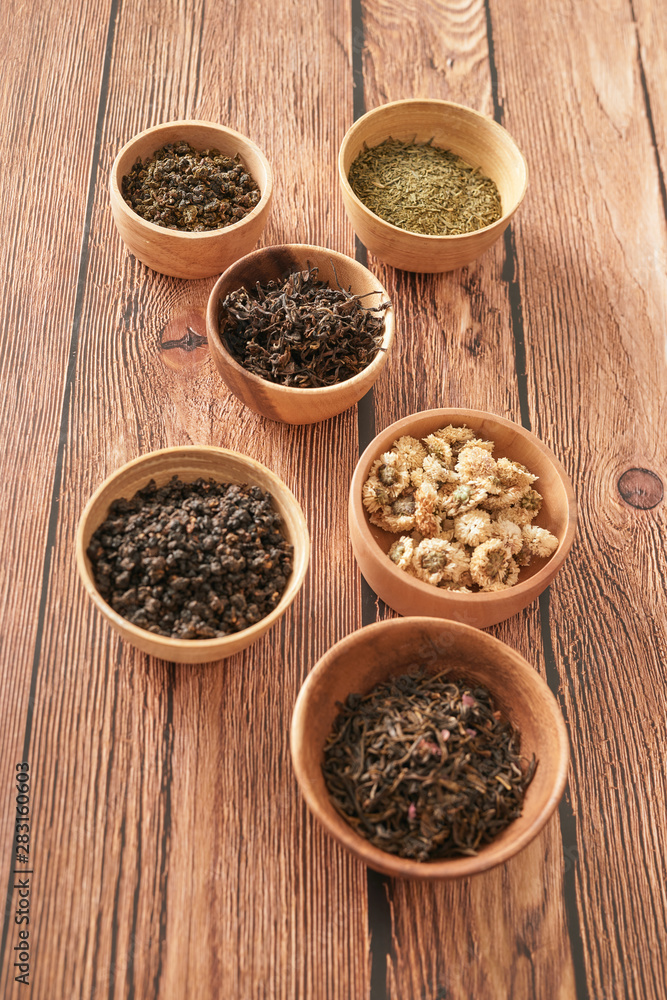 assortment of dry tea in white bowls on wooden surface