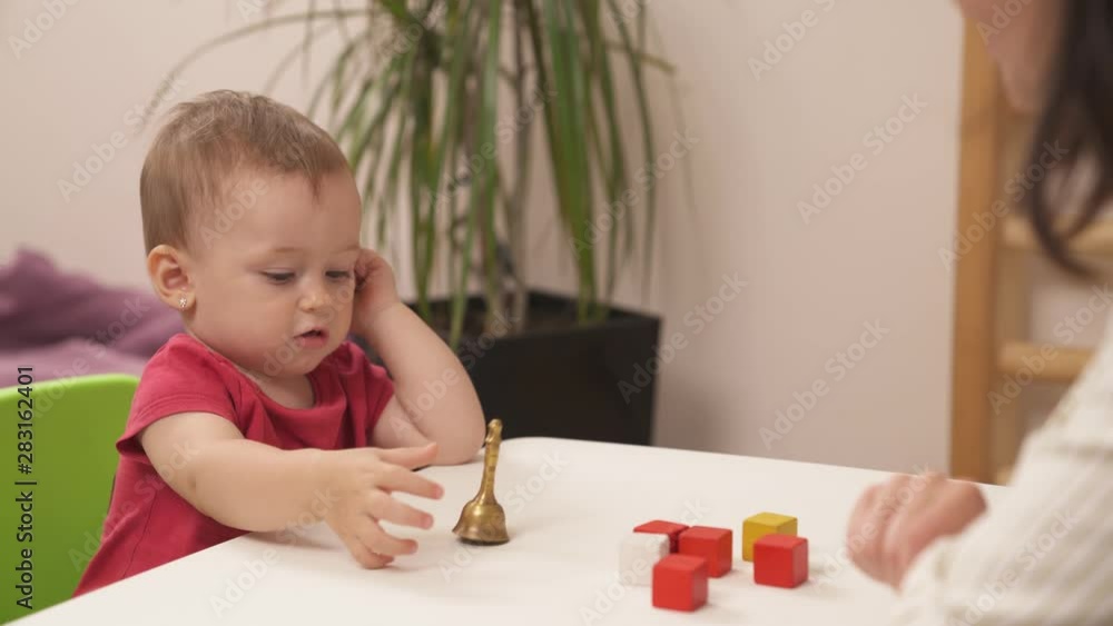 Little girl doing sensory exercises in playful form. Kid is playing with a bell. Development of kids fine motor skills concept. Educational toys.