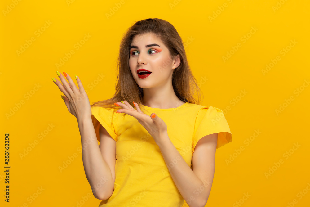Close-up portrait of a beautiful young girl pointing with a finger at the copyspace for product advertisement isolated over yellow background. Close-up portrait of a beautiful young girl pointing with a finger at the copyspace for product advertisement isolated over yellow background.