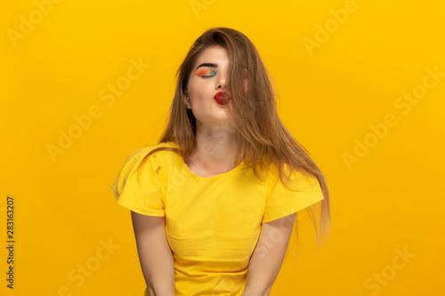 Close-up portrait of a beautiful kissing young girl isolated over yellow background.
