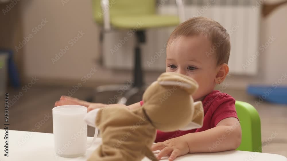 Close-up of toddler girl playing. Kid is giving a drink to a lovely puppet dog. Development of kids fine motor skills. Educational toys Close-up of toddler girl playing. Kid is giving a drink to a lovely puppet dog. Development of kids fine motor skills. Educational toys
