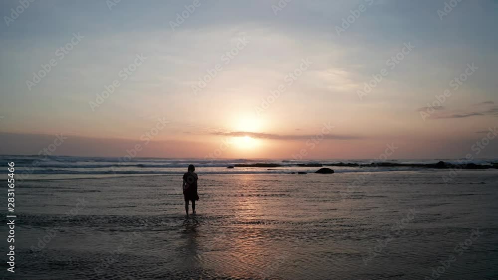 Silhouette of woman on the beach at beautiful sunset. Female relaxing on the black sand beach during sunset Silhouette of woman on the beach at beautiful sunset. Female relaxing on the black sand beach during sunset