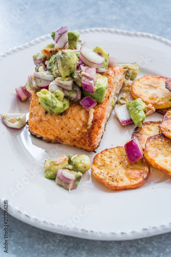 Salmon Fish Fillet with Avocado, Red Onions and Baked Round Potato Slices in Seafood Plate.