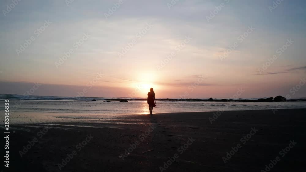 Silhouette of woman on the beach at beautiful sunset. Female relaxing on the black sand beach during sunset Silhouette of woman on the beach at beautiful sunset. Female relaxing on the black sand beach during sunset