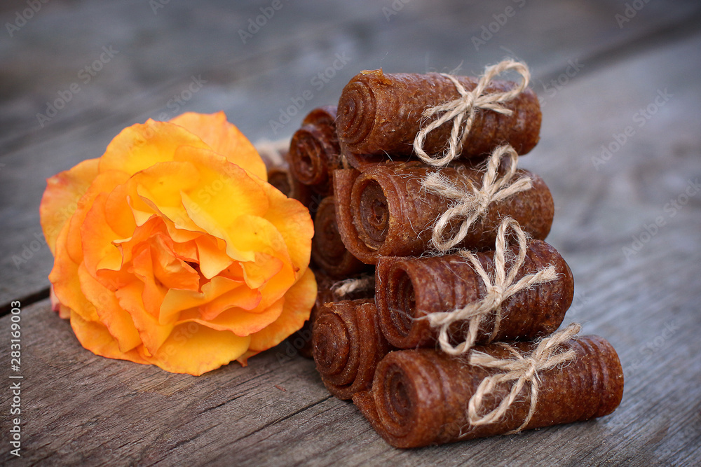 Handmade apple pastille rolled and tied with linen thread on a wooden background with an orange rose Handmade apple pastille rolled and tied with linen thread on a wooden background with an orange rose