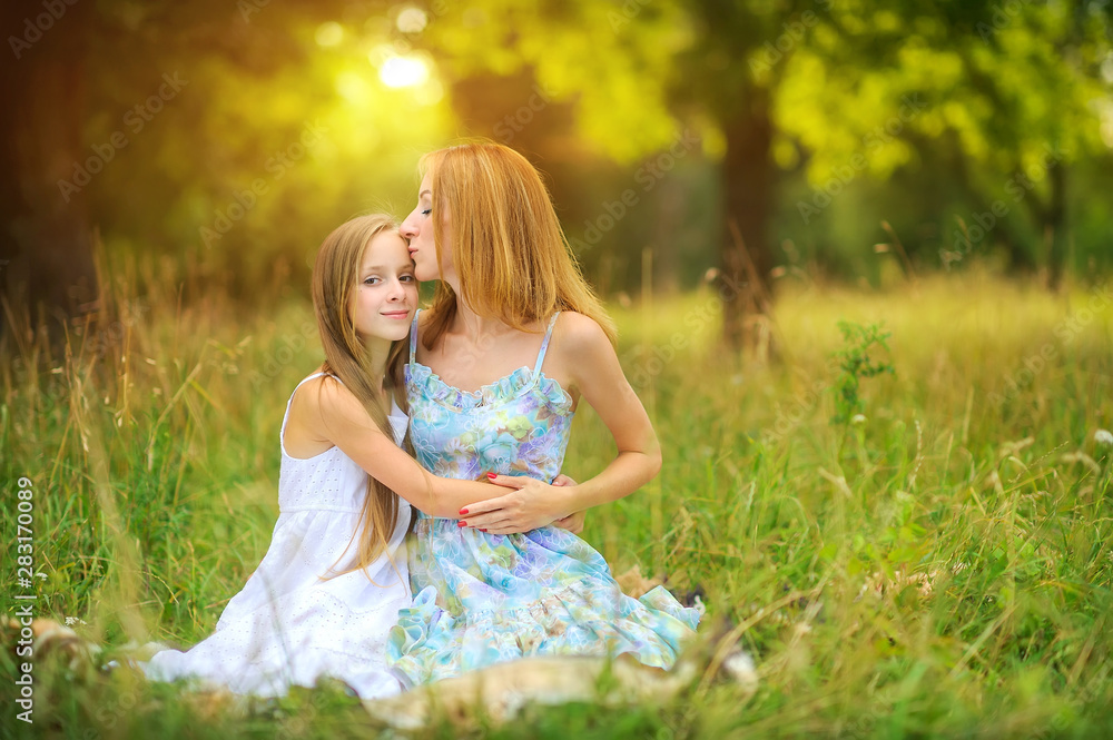 portrait of a happy mother with her daughter, sitting in the park on the grass, hugging and smiling, mother gently kisses her daughter, happy motherhood