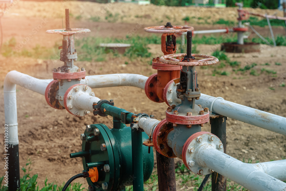 Oil and gas processing plant with pipe line valves. Oil pipeline valves in the oil and gas industry. Valve plug an oil pipeline in the field on a sunny summer day. Oil and gas processing plant with pipe line valves. Oil pipeline valves in the oil and gas industry. Valve plug an oil pipeline in the field on a sunny summer day.