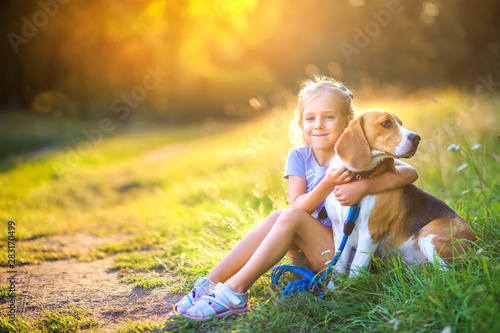 cute girl walks with her beagle puppy in the park at sunset, hugs and smiles, best friend