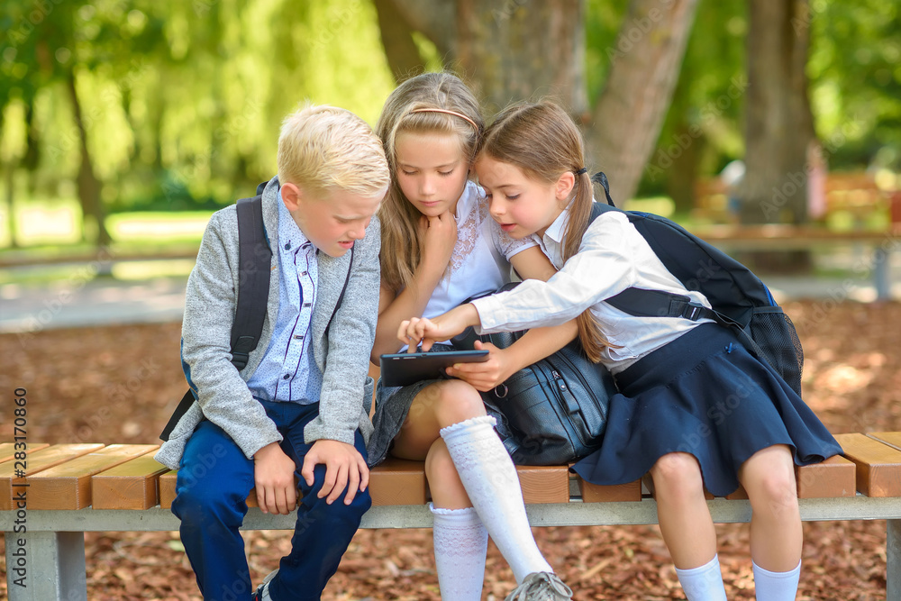 school friends, schoolchildren sitting on a bench in the park use a tablet, social media communication